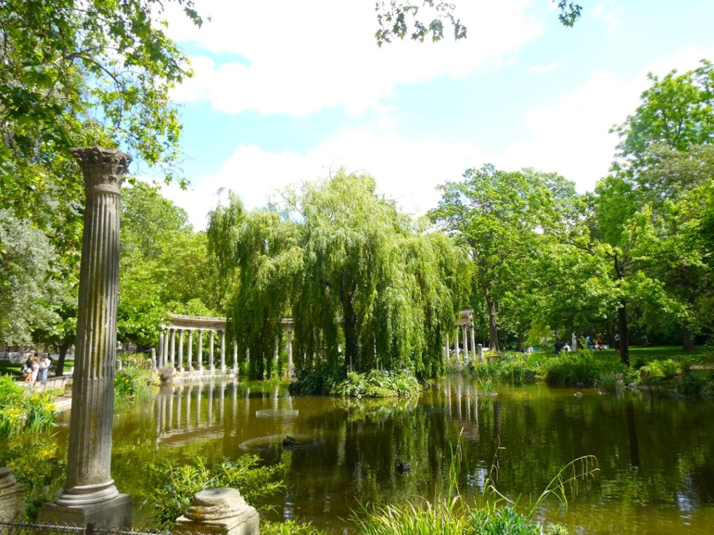 A serene pond with a weeping willow and ancient columns.